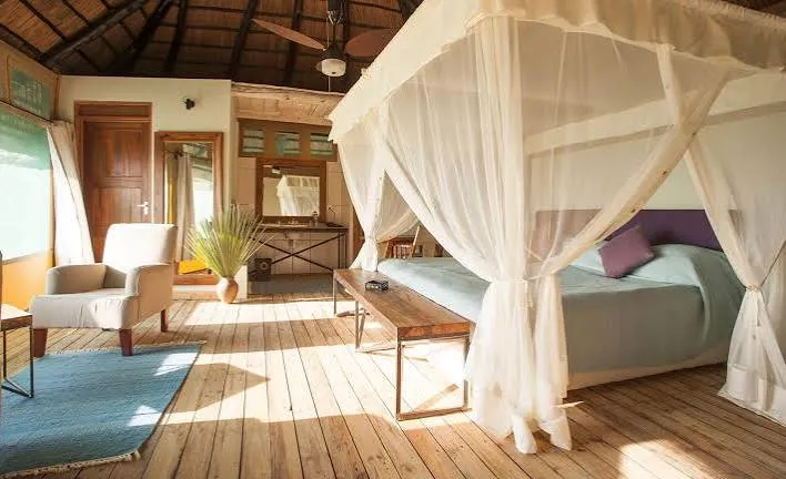 A four-poster bed under thatch in a light-filled tented suite