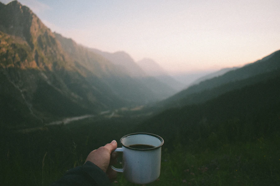 A mug of coffee held against a misty early-morning mountain view from camp